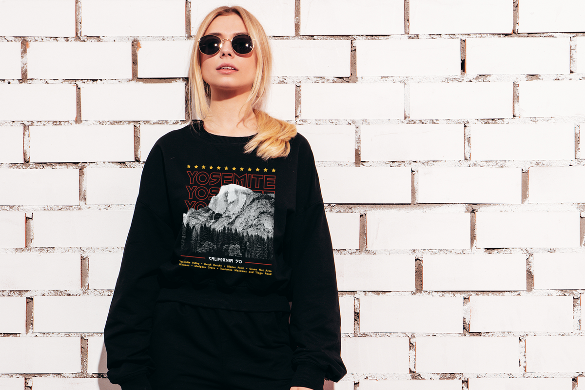 Person wearing a black sweatshirt with a 'Yosemite'  graphic design against a white brick wall